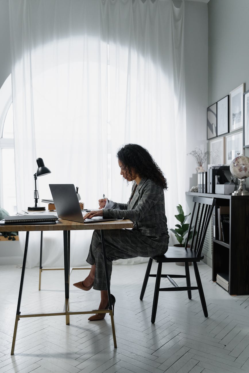 Woman gently stretching her wrist while sitting at a wooden desk with a laptop.